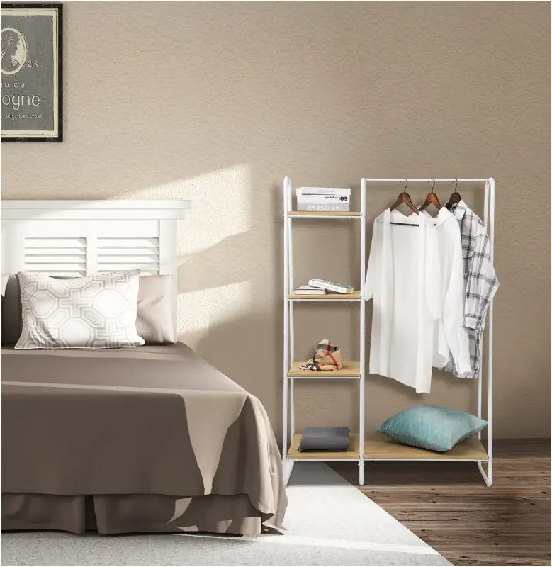 Wit kledingrek met planken naast een bed, ingericht met kleding, boeken en een groen kussen