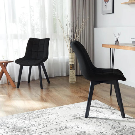 Twee zwarte fluwelen eetkamerstoelen met houten poten in een woonruimte, één van voren en één van opzij