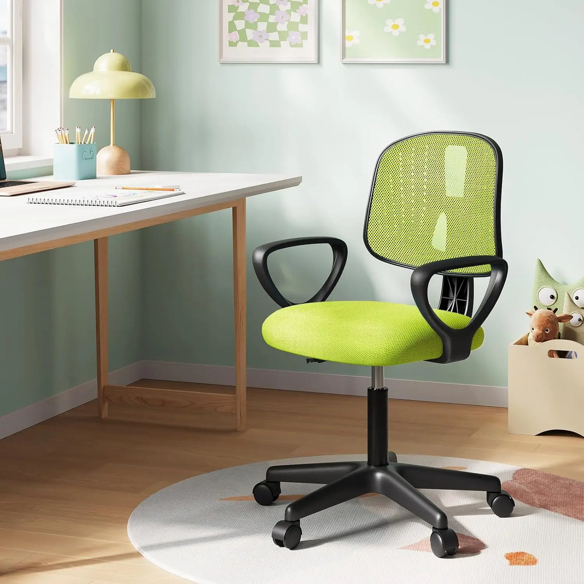 Groene kinderbureaustoel met armleuningen en vijf wielen naast een bureau in een kinderkamer