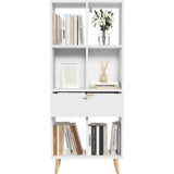 Witte boekenkast met zes open vakken, een lade en houten poten, gevuld met boeken en decoratie