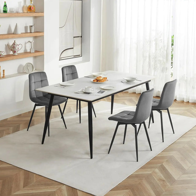 Vier donkergrijze velvet eetkamerstoelen met zwarte poten rond een witte eettafel